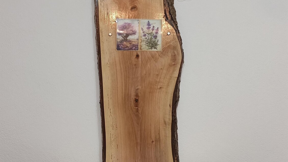 Ein rustikaler Holztisch mit einer schönen Tischdecke in Lavendeldesign. Auf der Wand im Hintergrund hängen Bilder von Lavendel. | © Fam. Tomaschitz