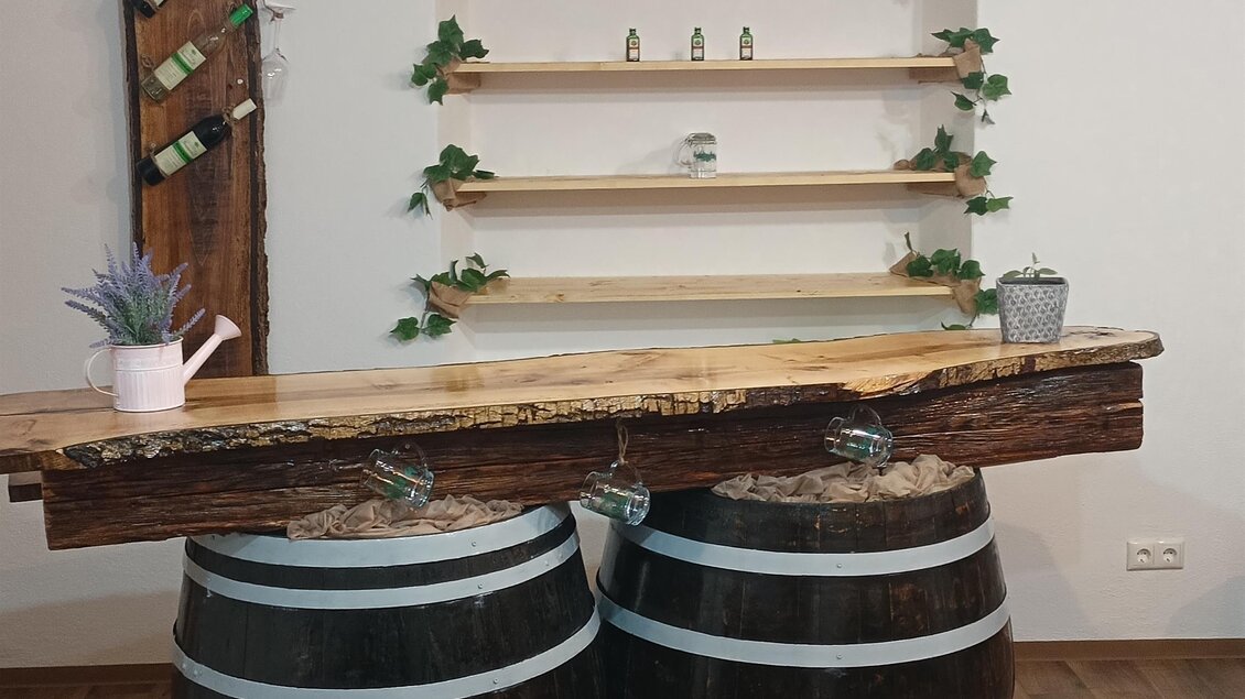 Ein rustikaler Thekenbereich mit zwei Weinfässern als Tisch. Im Hintergrund befindet sich ein Regal mit Pflanzen und Dekoration. | © Fam. Tomaschitz
