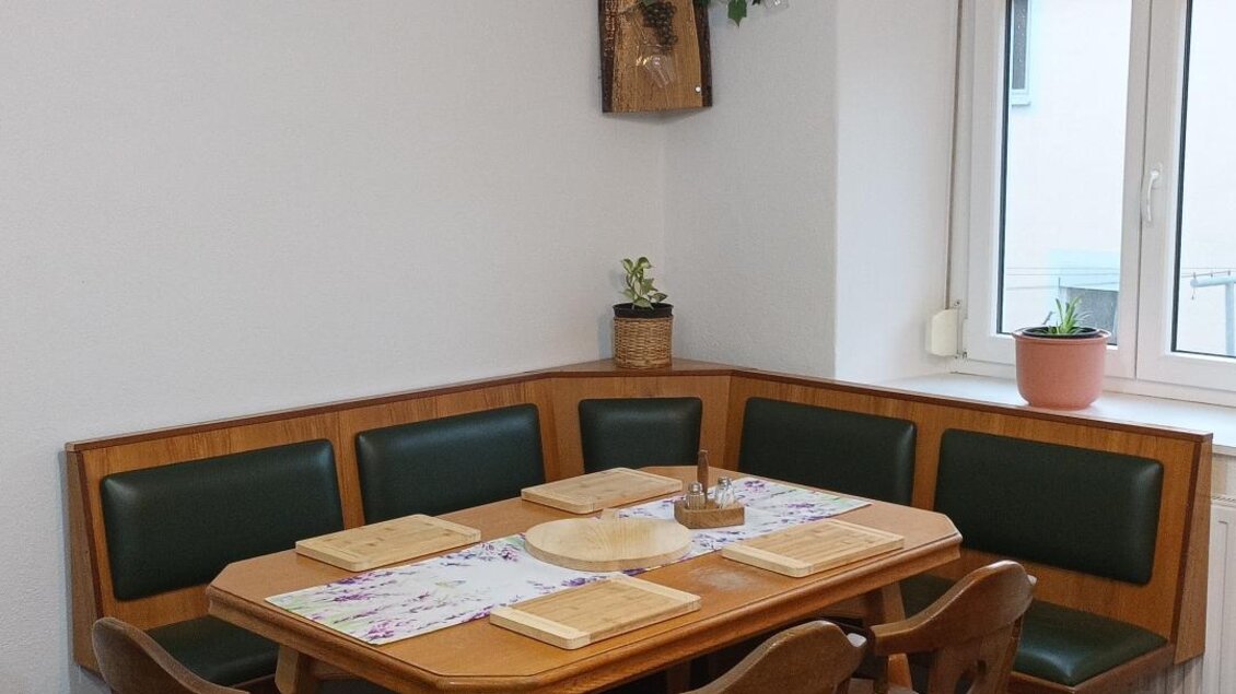 Ein gemütlicher Essbereich mit einer Holzbank und einem Tisch. Die Wände sind hell und es gibt Pflanzen zur Dekoration. | © Fam. Tomaschitz