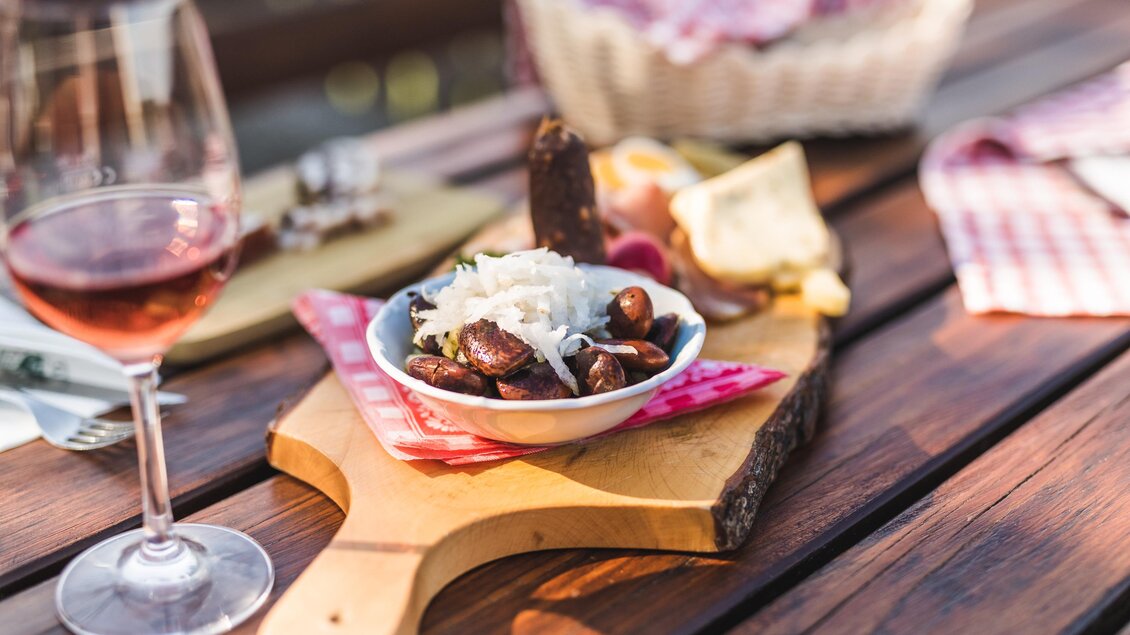 Ein schöner Tisch mit einer Auswahl an Snacks und einem Glas Roséwein. Im Vordergrund befindet sich eine Schüssel mit Oliven und Käse auf einer Holzplatte. | © Die Abbilderei