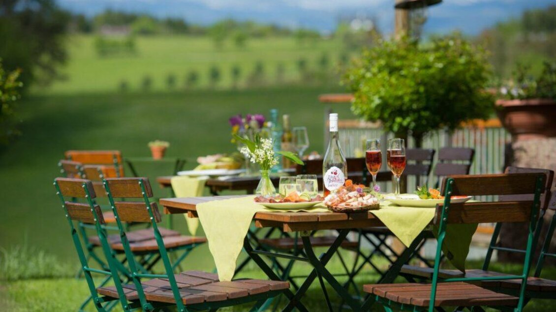 Ein einladender Tisch im Freien, gedeckt mit köstlichen Speisen und Getränken. Im Hintergrund erstreckt sich eine grüne Landschaft unter blauem Himmel. | © HP Dornerwein