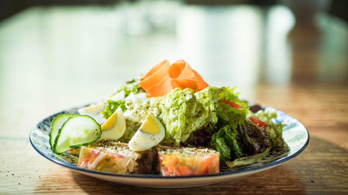 Ein Teller mit frisch zubereitetem Salat aus dem Buschenschank Dorner, garniert mit gekochten Eiern, Gurkenscheiben und Karotten. Die Salatmischung enthält verschiedene Blattsalate und wird auf einem dekorativen Teller serviert. | © Strobl Christa