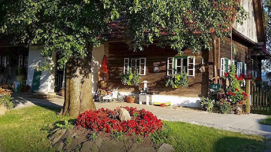 Ein wunderschönes Holzhaus mit bunten Blumen und einem gepflegten Garten. Die Umgebung ist grün und einladend. | © Buschenschank Eckfastl