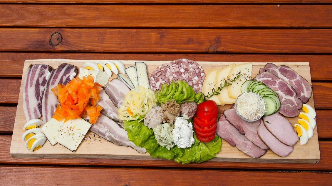 Ein großes Brett mit verschiedenen Wurst- und Käsesorten, garniert mit Gemüse. Die platzierten Zutaten sind farbenfroh und appetitlich angerichtet. | © Buschenschank Eckfastl