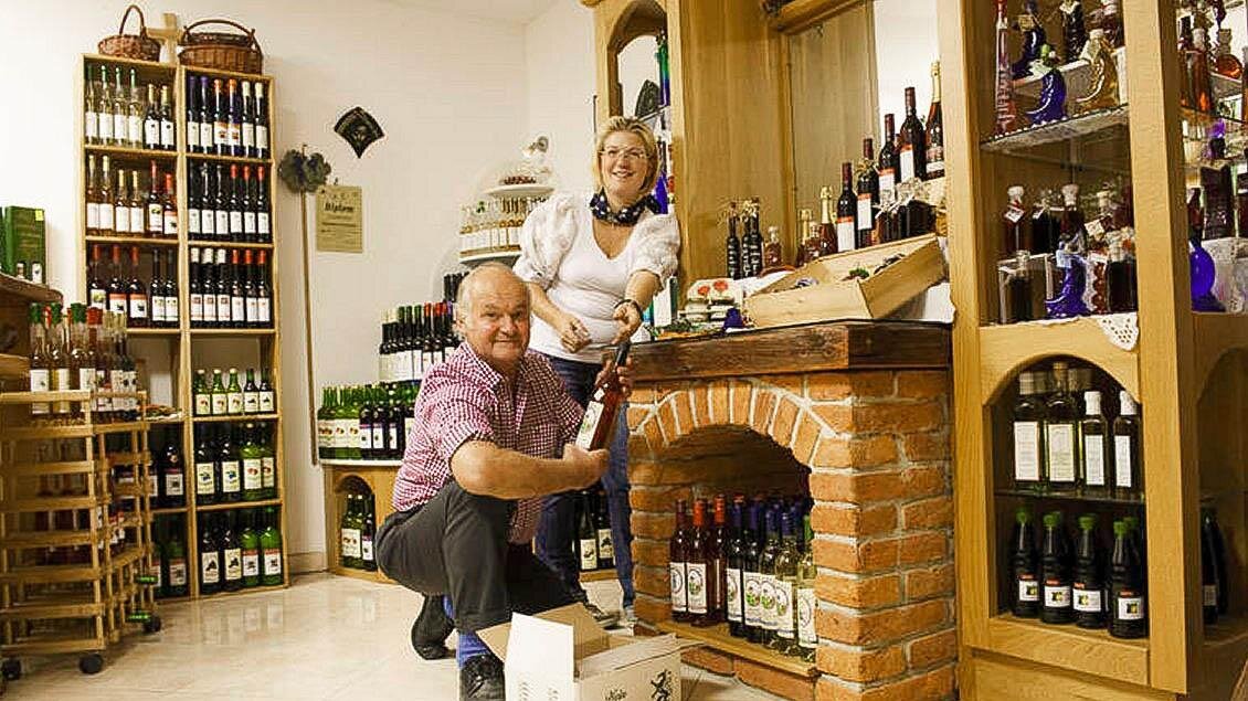 Ein Weinladen mit Regalen voller Flaschen. Ein älteres Paar steht am Verkaufstresen und bietet Wein an. | © Buschenschank Eckfastl