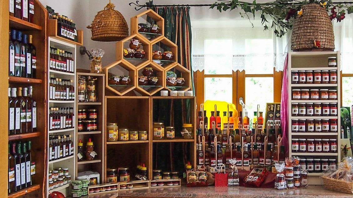 Ein gemütlicher Laden voller Gewürze und Konfitüren in Regalen. Bienenstock-ähnliche Ständer zeigen Honigprodukte und handgefertigte Leckereien. | © Buschenschank Eckfastl