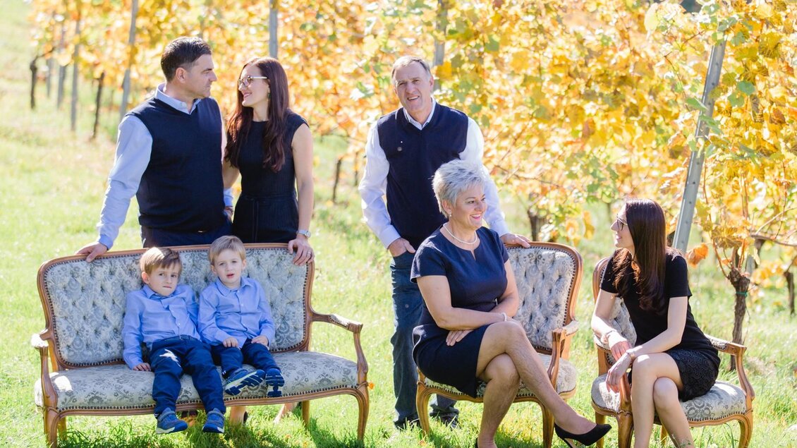 Eine Familie posiert in einem Weinberg. Im Hintergrund sind gelbe Blätter und ein sonniger Himmel zu sehen. | © Weingut Elsnegg