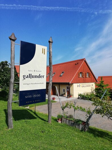 Ein modernes weißes und rotes Gebäude mit einem Schild, das "gallunder" anzeigt. Der Himmel ist blau und der Garten ist grün gestaltet. | © Sabine Gallunder