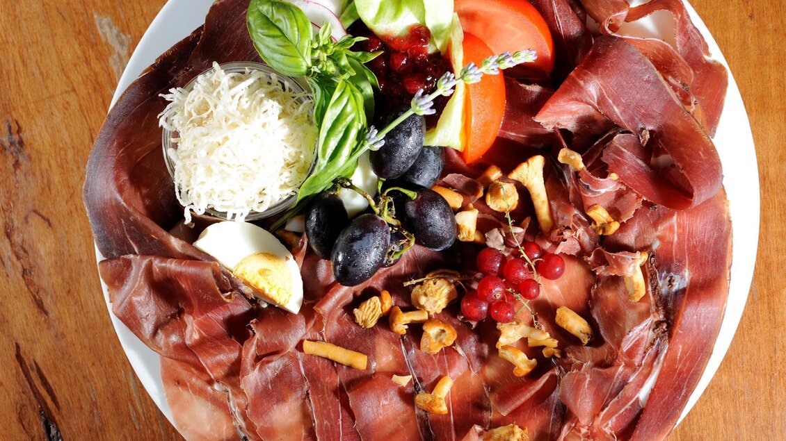 Ein Teller mit verschiedenen Wurst- und Käsesorten, garniert mit frischem Gemüse und Trauben. Die Anordnung ist ansprechend und wirkt appetitlich. | © Weingut Gerngross