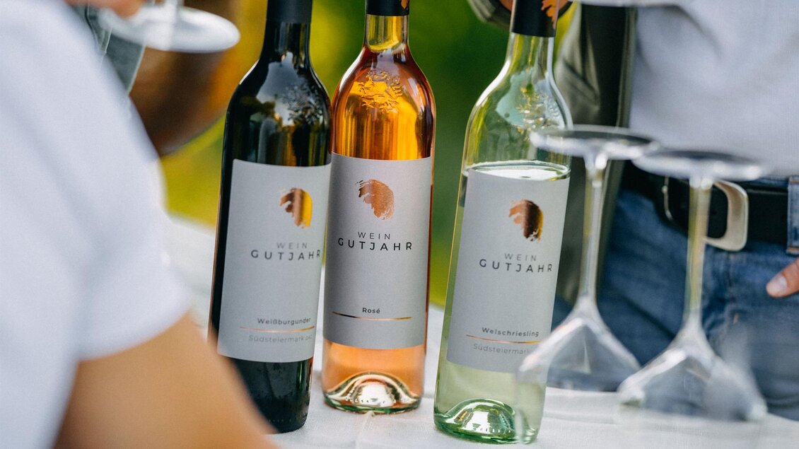 Drei Flaschen Wein stehen auf einem Tisch, begleitet von Weingläsern. Die Flaschen zeigen unterschiedliche Farben: Rot, Rosé und Weiß. | © Weingut Gutjahr