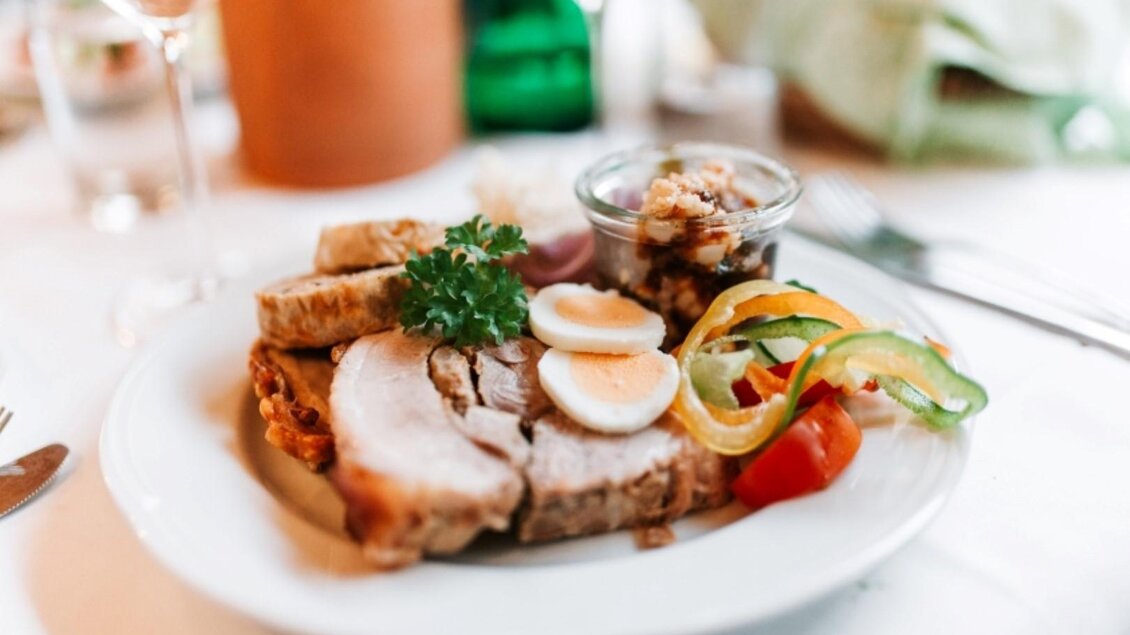 Ein Teller mit verschiedenen Fleischsorten, Eiern und buntem Gemüse. Im Hintergrund sind Gläser und eine Grünfläche zu sehen. | © Weingut Gutjahr