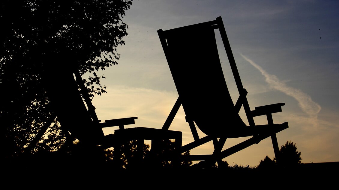 Zwei Liegestühle silhouettiert gegen den Sonnenuntergang. Im Hintergrund sind Bäume und ein weicher Himmel zu sehen. | © Thermen- und Vulkanland