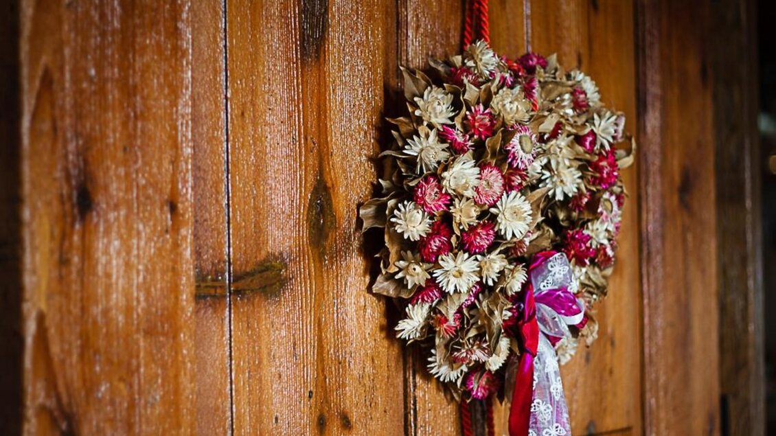 Ein schöner Türkranz aus getrockneten Blumen und Bändern. Der Kranz hängt an einer rustikalen Holzoberfläche. | © Hack-Gebell