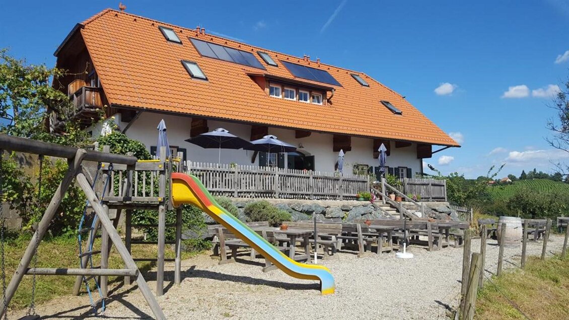 Ein modernes Haus mit rotem Dach und großen Fenstern. Vor dem Haus befindet sich ein Spielplatz mit einer bunten Rutsche. | © Hack-Gebell