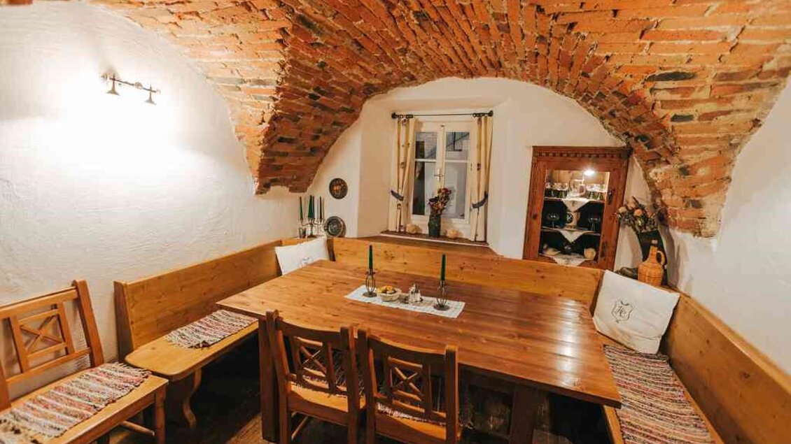 Ein gemütlicher Essbereich mit einem großen Holztisch und Bänken. Die Wände sind aus Ziegelsteinen und die Beleuchtung ist sanft. | © Hack-Gebell