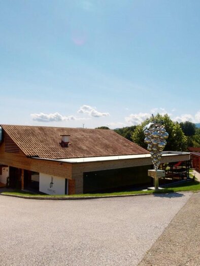 Ein malerisches Gebäude in einer ländlichen Umgebung, umgeben von grünen Hügeln. Der Himmel ist blau mit wenigen Wolken. | © Buschenschank Pichlippi