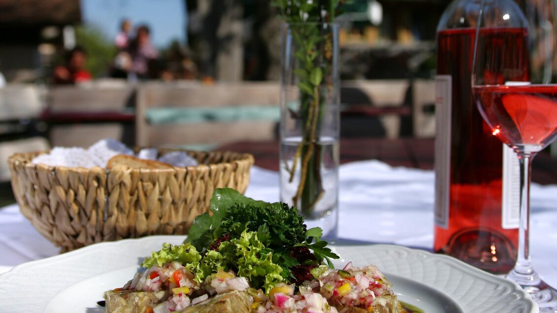 Ein schön angerichtetes Gericht mit frischem Gemüse und Salat auf einem weißen Teller. Im Hintergrund stehen eine Flasche Roséwein und ein Korb mit Brot. | © Graz Tourismus - Harry Schiffer