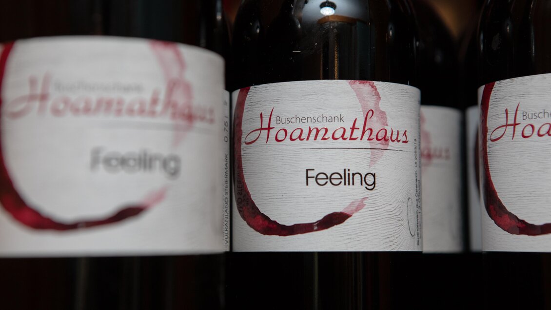 Einige Flaschen Wein mit dem Etikett "Feeling" und dem Schriftzug "Buschenschank Hoamathaus". Die Flaschen stehen nebeneinander und haben ein ansprechendes Design. | © GlaMUR-Genuss am Fluss