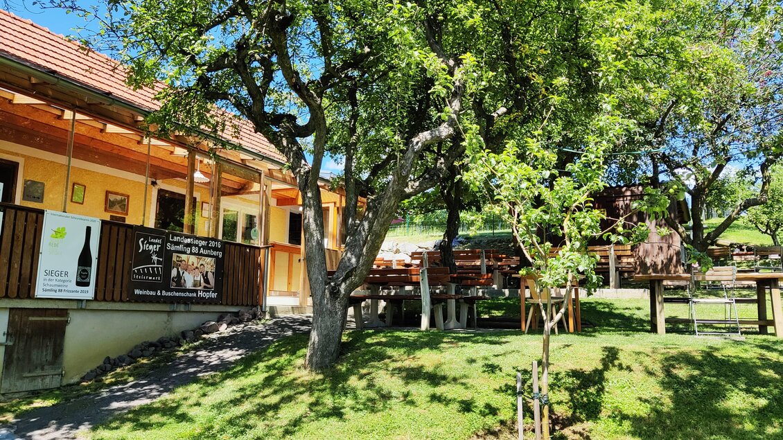 Ein gemütliches Restaurant umgeben von Bäumen und grünem Gras. Auf der Terrasse stehen Tische im Freien.