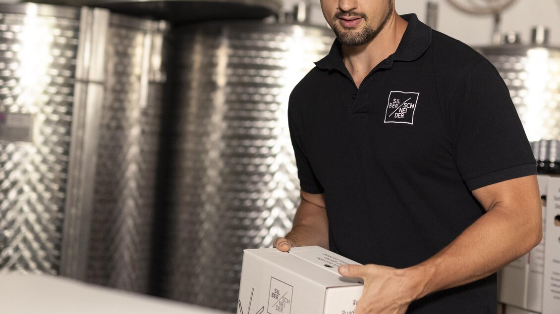 Ein Mann in einem Lagerraum trägt eine Kiste. Im Hintergrund sind silberne Tanks und Flaschen zu sehen. | © Lisa Resatz_Moonpower