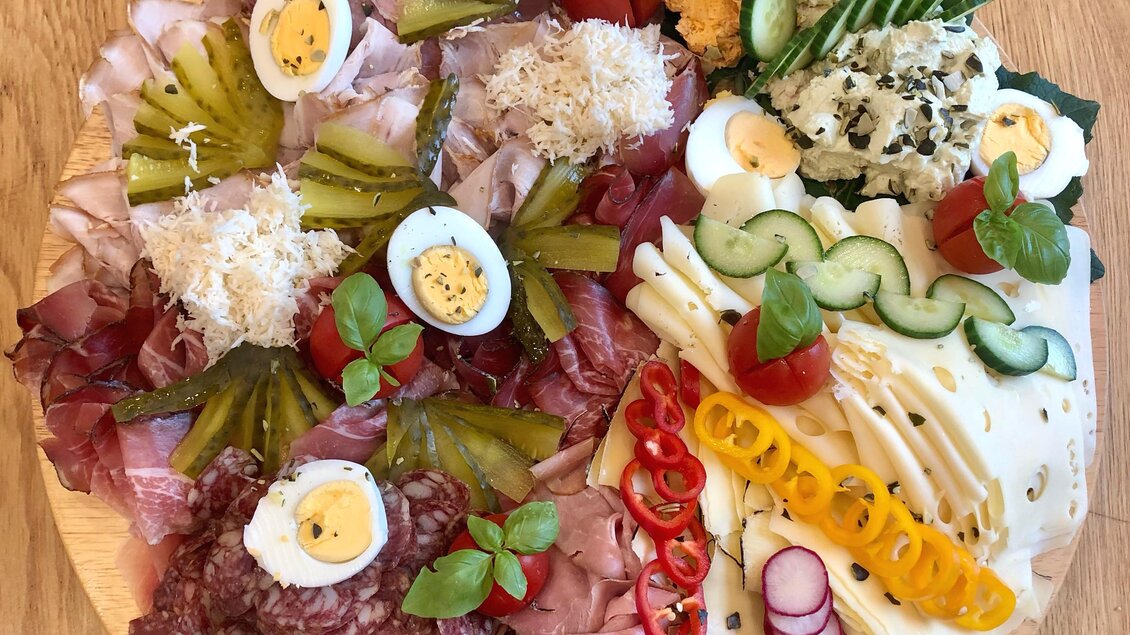 Eine vielfältige Fleisch- und Käseplatte auf einem Holzbrett, dekoriert mit Gemüse und Eiern. Bunte und frische Zutaten machen das Gericht ansprechend. | © Brigitte Maier | Klapotetzhof Silberschneider