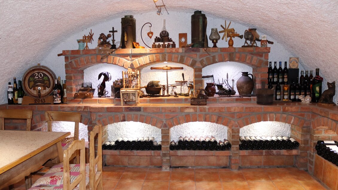 Ein gemütlicher Weinkeller mit einer Steinmauer und vielen Weinflaschen. Dekorative Vintage-Objekte fügen einen rustikalen Charme hinzu. | © Klapotetzhof Silberschneider