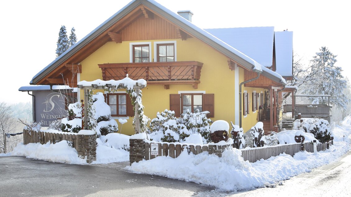 Ein schönes, gelbes Haus im Schnee mit einem hellen Himmel. Der Garten ist mit Schnee bedeckt und die Atmosphäre ist winterlich und gemütlich. | © Klapotetzhof Silberschneider