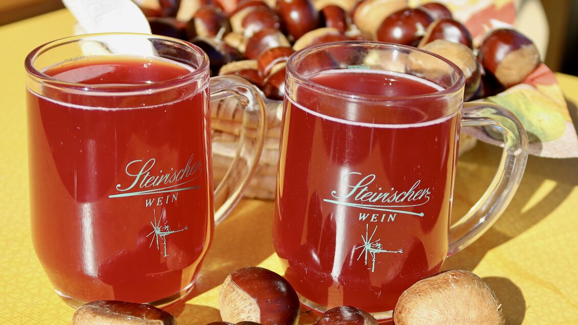 Zwei Gläser mit Glühwein stehen auf einem gelben Tisch, umgeben von Kastanien. Im Hintergrund sieht man einen Korb mit mehr Kastanien. | © Klapotetzhof Silberschneider