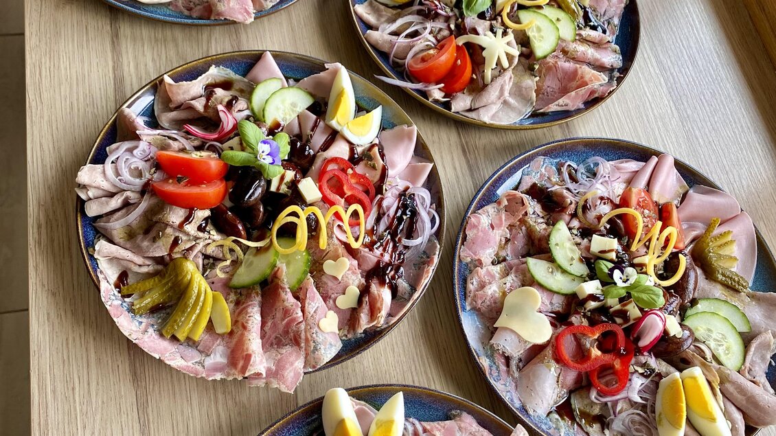 Sechs Teller mit buntem Aufschnitt und verschiedenen Gemüsesorten sind arrangiert. Die dekorativen Elemente verleihen den Tellern ein ansprechendes Aussehen.