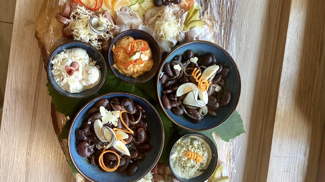 Eine kunstvoll arrangierte Platte mit verschiedenen Käsesorten, Aufschnitt, Obst und Gemüse. In mehreren Schalen sind Snacks und Dips hübsch angerichtet.