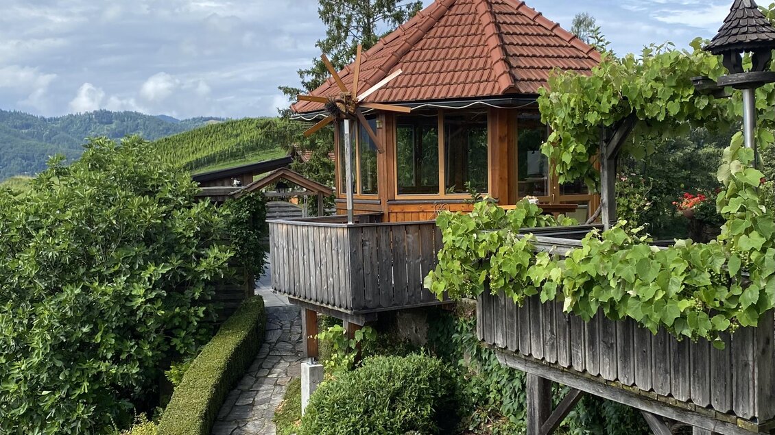 Ein hübsches Holzhaus mit rotem Dach, umgeben von üppigem Grün. Der Weg führt durch einen schönen Garten mit bunten Pflanzen.