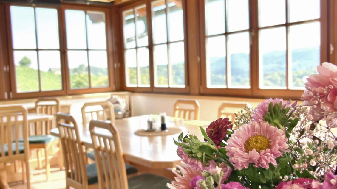 Ein helles und einladendes Esszimmer mit großen Fenstern und Holzmöbeln. Ein wunderschönes Blumengesteck sorgt für eine freundliche Atmosphäre. | © Brigitte Maier | Klapotetzhof Silberschneider