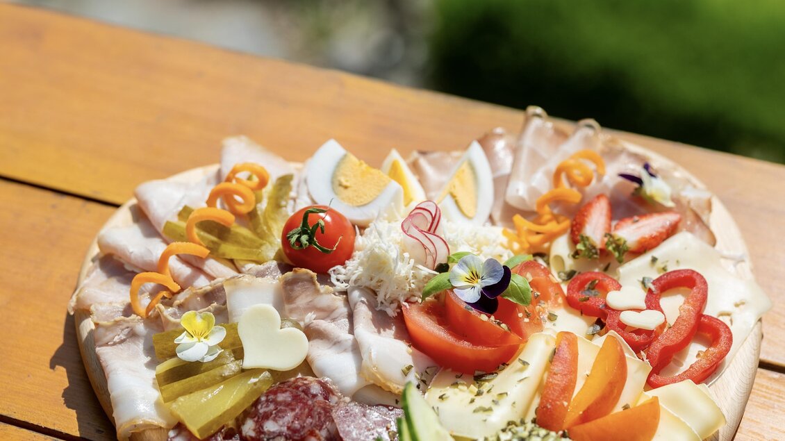 Ein herzförmiger Teller mit verschiedenen Aufschnittsorten, Käsestücken, frischem Gemüse und Dekoration. Die bunten Zutaten sind appetitlich angerichtet und laden zum Genießen ein. | © © RMSW GmbH/ Nikola Milatovic