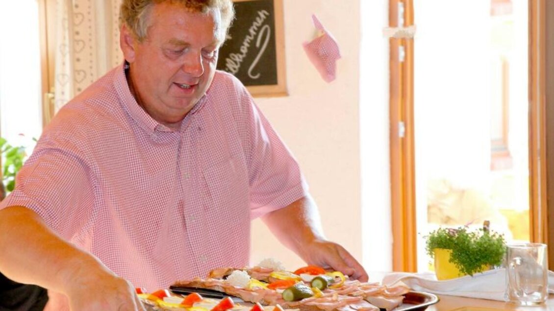 Ein Mann serviert eine Platte mit verschiedenen Speisen. Die Atmosphäre ist freundlich und einladend. | © Familie Kober
