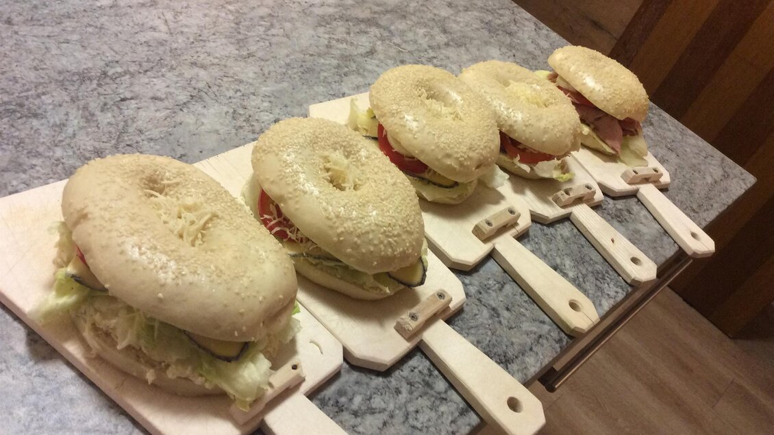 Fünf frisch zubereitete Bagels auf kleinen Holzbrettchen. Jeder Bagel ist mit frischem Gemüse wie Salat und Tomaten belegt. | © Weingut Koller