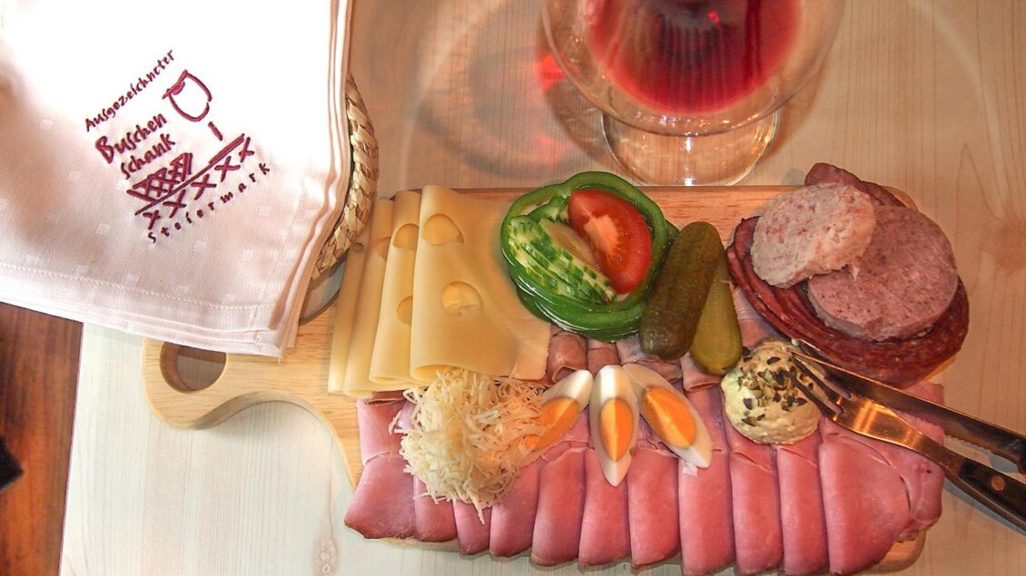 Eine appetitliche Auswahl an Wurst, Käse und Gemüse auf einem Holzbrett. Im Hintergrund steht ein Glas mit einem erfrischenden Getränk. | © Marion & Peter Labanz | Buschenschank Labanz