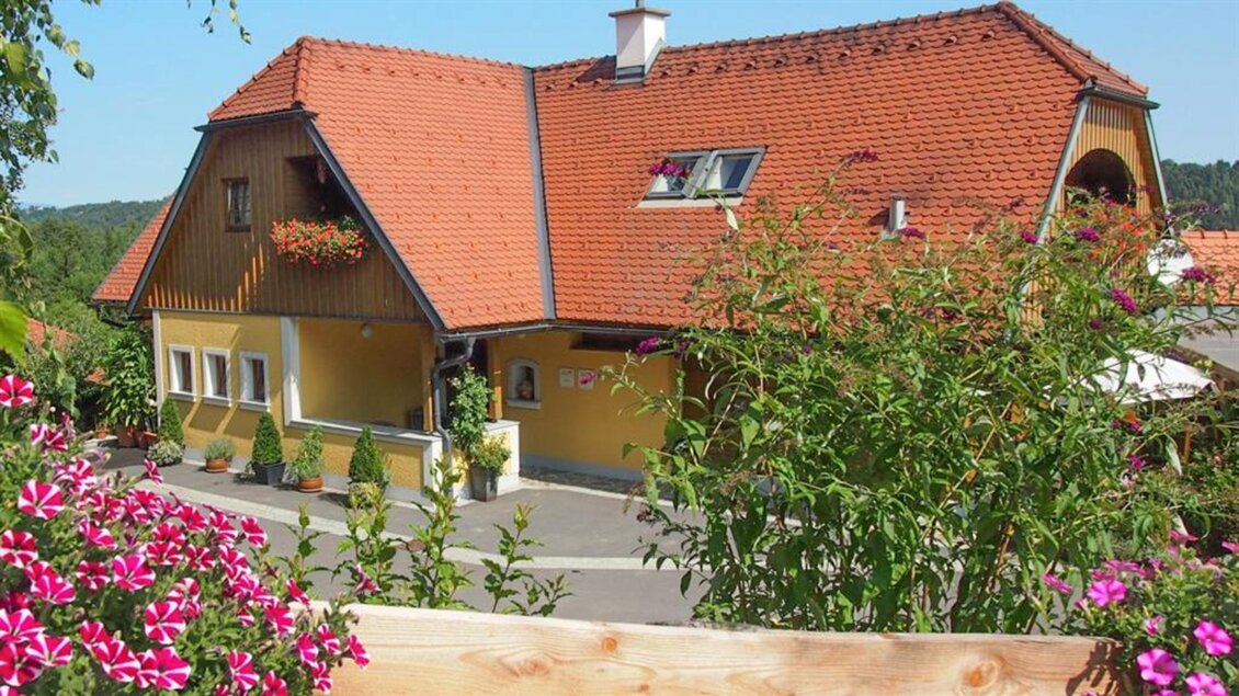 Ein schönes gelbes Haus mit einem roten Dach und grünen Pflanzen im Vordergrund. Die Umgebung ist hell und einladend. | © Marion & Peter Labanz | Buschenschank Labanz