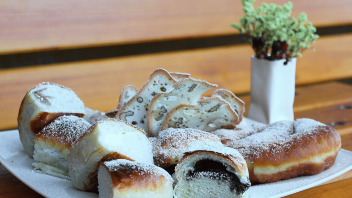 Ein Teller mit verschiedenen Backwaren, darunter süße Teilchen und gefüllte Brötchen. Im Hintergrund steht ein kleiner Blumentopf. | © Marion & Peter Labanz | Buschenschank Labanz