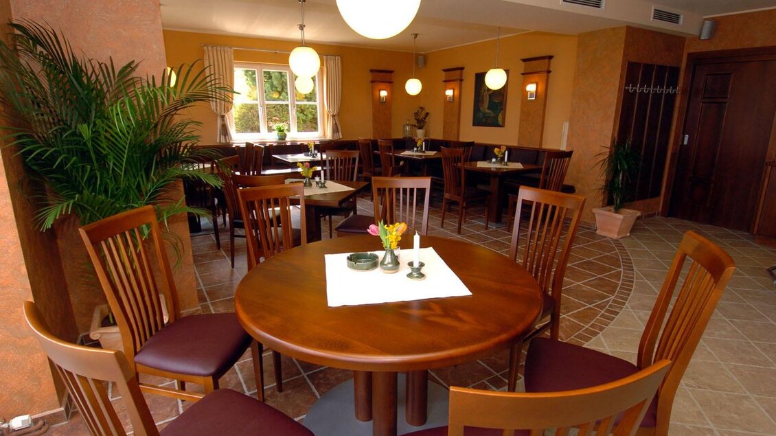 Ein gemütliches Restaurant mit holzfarbenen Tischen und Stühlen. Die Wände sind orange, und es gibt Pflanzen sowie runde Laternen, die eine einladende Atmosphäre schaffen. | © Weingut Lambauer
