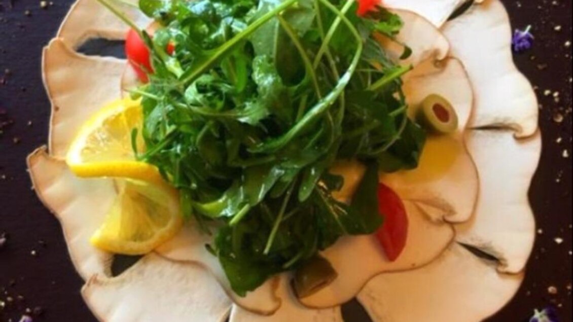 Ein schön angerichteter Salat mit frischem Grün, Zitronenscheiben und kleinen Tomaten. Die Blätter liegen auf einer dekorativen Anordnung von Pilzscheiben. | © Weingut Lambauer