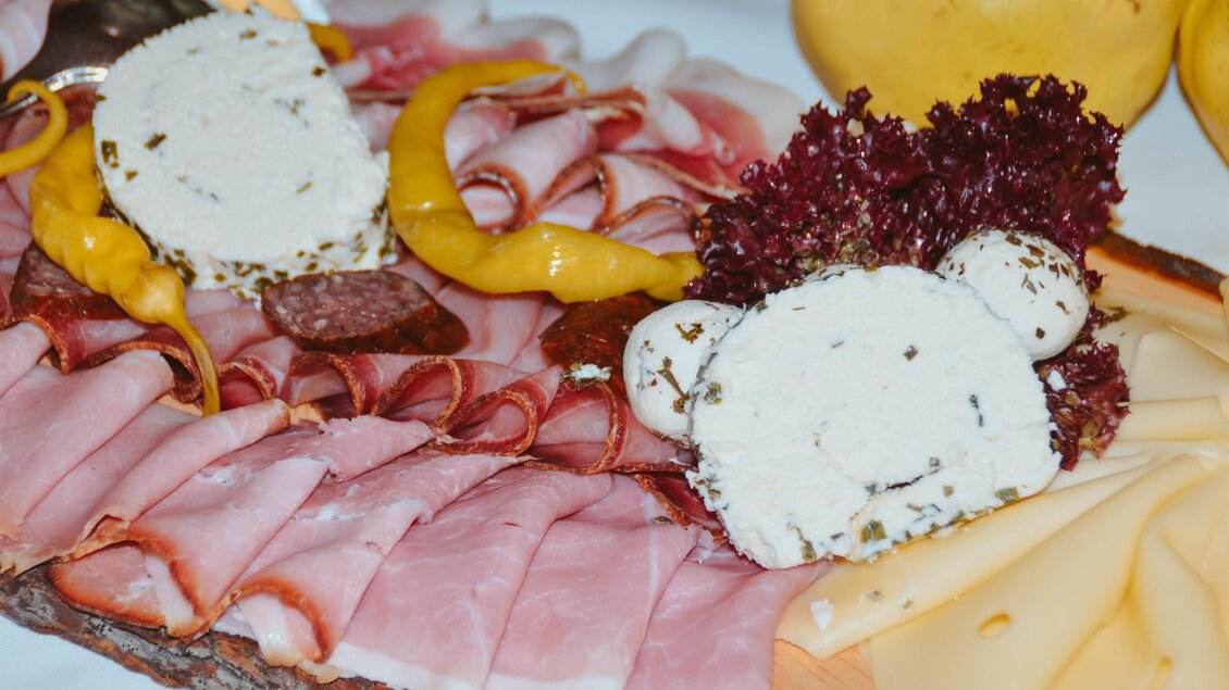 Ein köstliches Wurst- und Käsebrett mit verschiedenen Fleischsorten und frischen Beilagen. Attraktiv angerichtet mit Kräuterfrischkäse und buntem Gemüse.