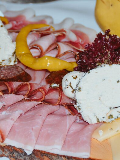 A delicious sausage and cheese platter with various types of meat and fresh side dishes. Attractively arranged with herb cream cheese and colorful vegetables.