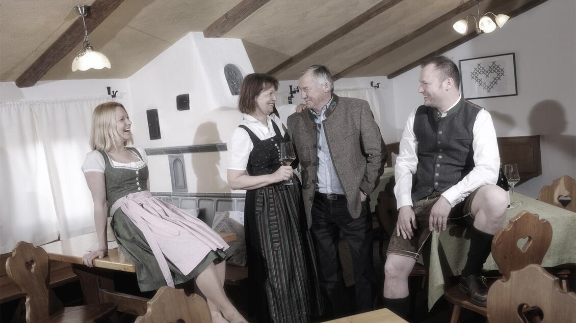 Eine gesellige Runde in einem gemütlichen Gastraum. Menschen in traditioneller bayerischer Tracht unterhalten sich. | © www.michilorenz.at