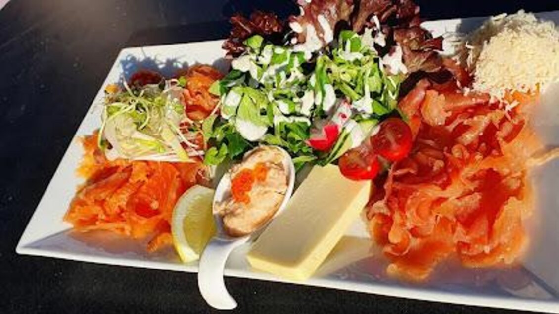 Ein schön angerichteter Teller mit Räucherlachs, Salat, frischen Kräutern und einer Zitronenscheibe. Dazu gibt es Käse und eine kleine Schale mit Dip. | © Gerhard Maurer