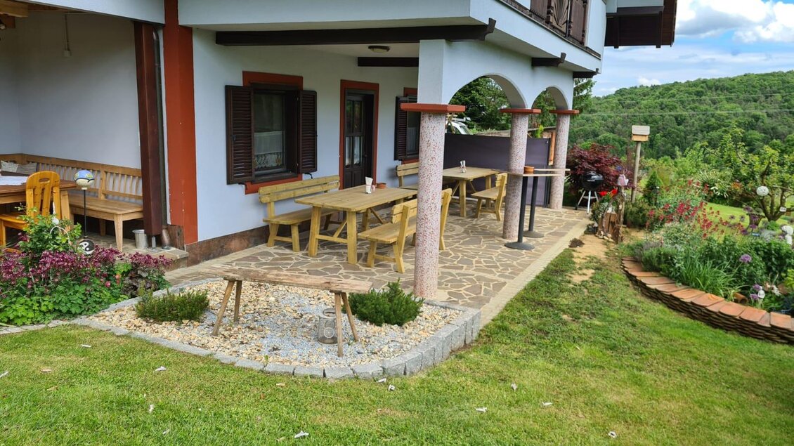 Ein gemütlicher Außenbereich mit Holztischen und Stühlen, umgeben von schönen Pflanzen. Der Platz bietet einen Blick auf eine grüne Landschaft. | © Gerhard Maurer