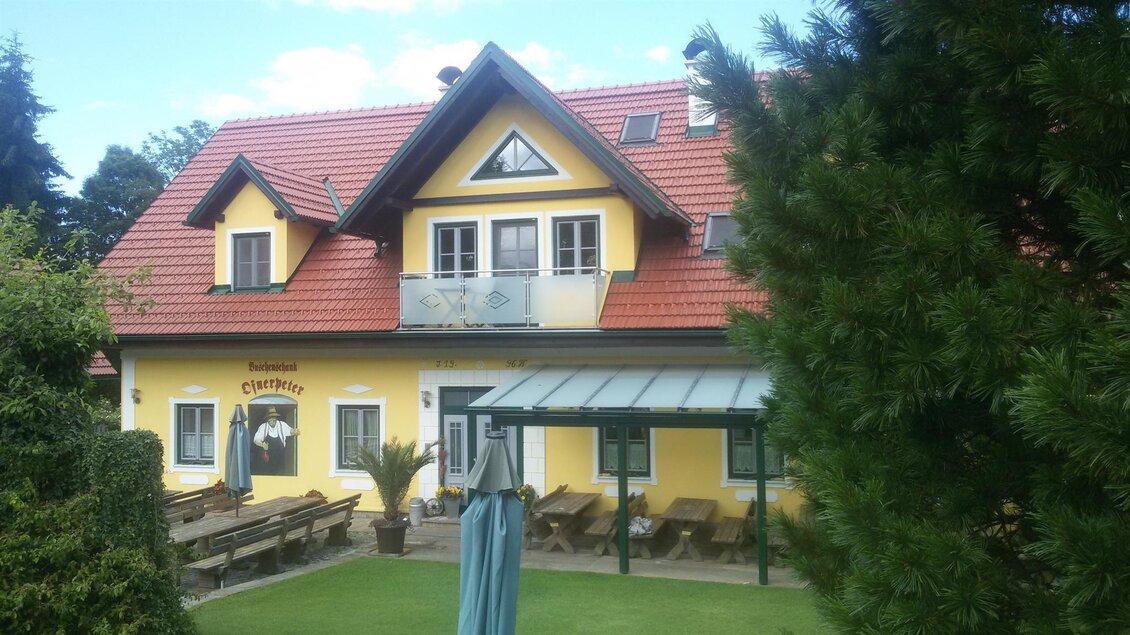 Ein hübsches Haus mit gelber Fassade und rotem Dach. Vor dem Haus befinden sich eine Terrasse und Sitzgelegenheiten im Freien. | © Ofnerpeter