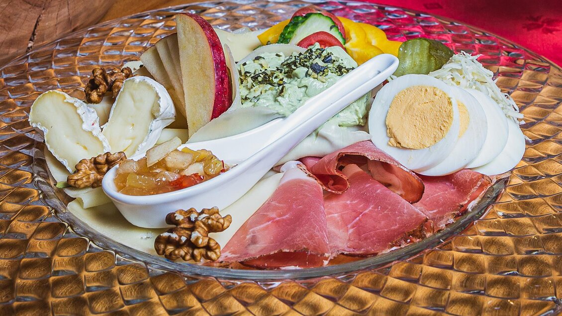 Ein kunstvoll angerichteter Teller mit verschiedenen Käsesorten, Schinken, Obst und Nüssen. Dazu gibt es eine Schale mit eingemachtem Obst und ein hartgekochtes Ei. | © Weingut Pölzl
