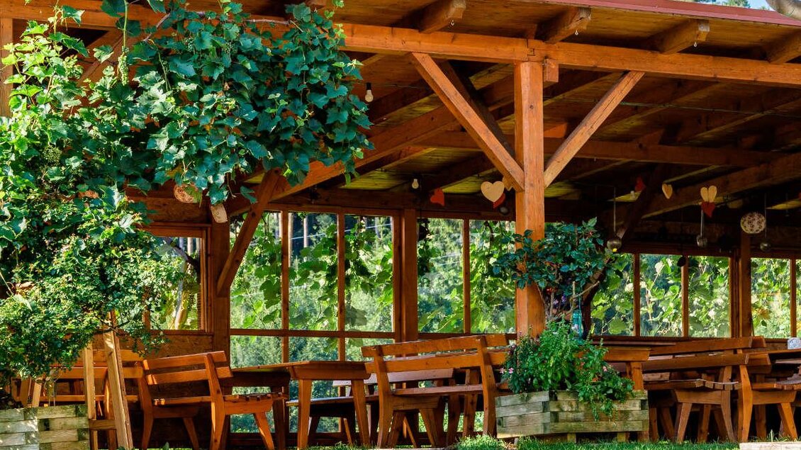 Ein gemütlicher Holzpavillon mit vielen Tischen und Bänken. Umgeben von Pflanzen und einem schönen Garten. | © Weinbau Pühringer