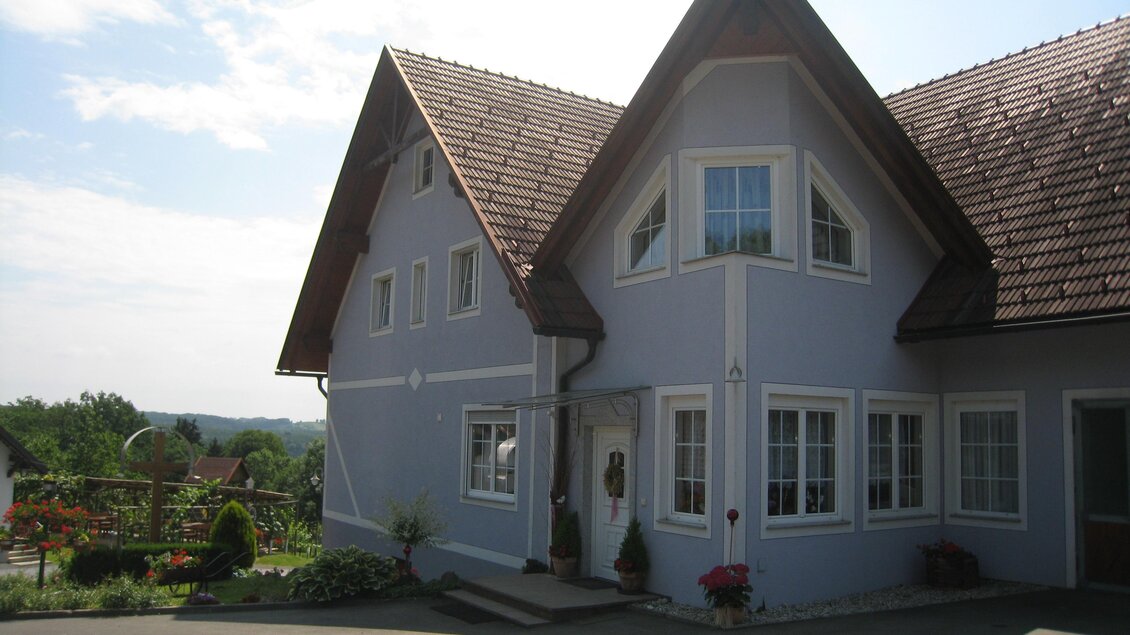 Ein charmantes Haus mit einer attraktiven Dachform und hellblauer Fassade. Der Garten ist gepflegt und bietet eine schöne Aussicht auf die Umgebung. | © Buschenschank Paierl