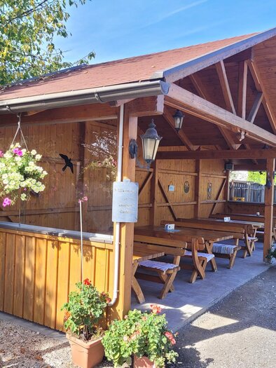 A cozy wooden pavilion with a table and benches outdoors. Flower baskets give the place an inviting atmosphere. | © TV Südsteiermark - Irene Löschnig